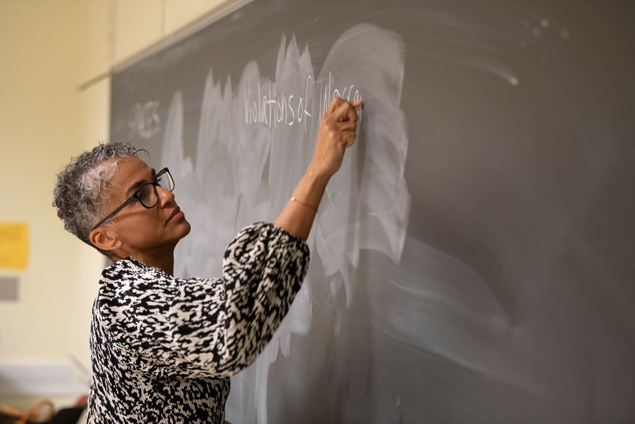 Female professor writes on chalkboard with back to classroom.