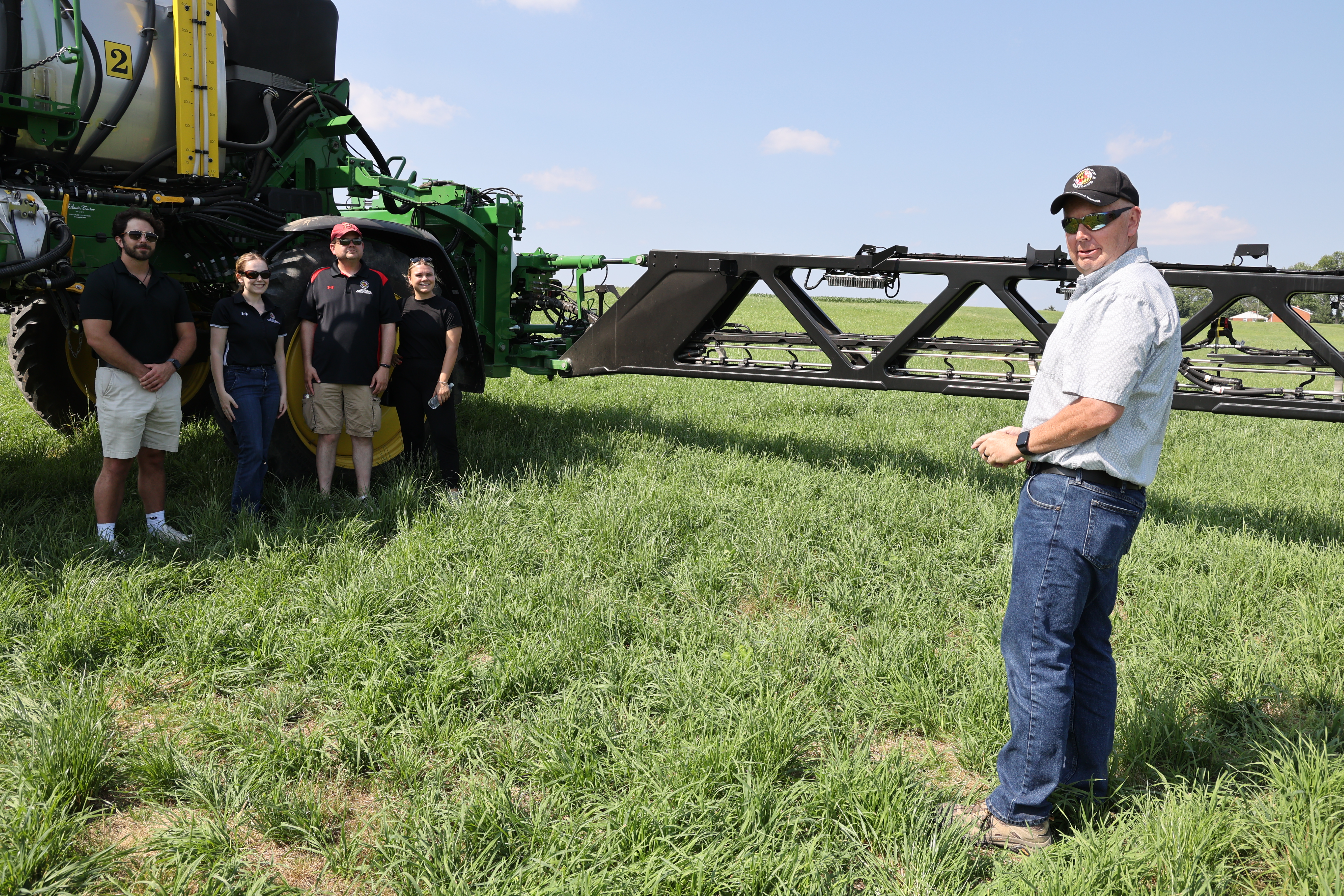 Farmer and UM Scholars pictured with their faculty mentor in a field, in front of a large tractor.