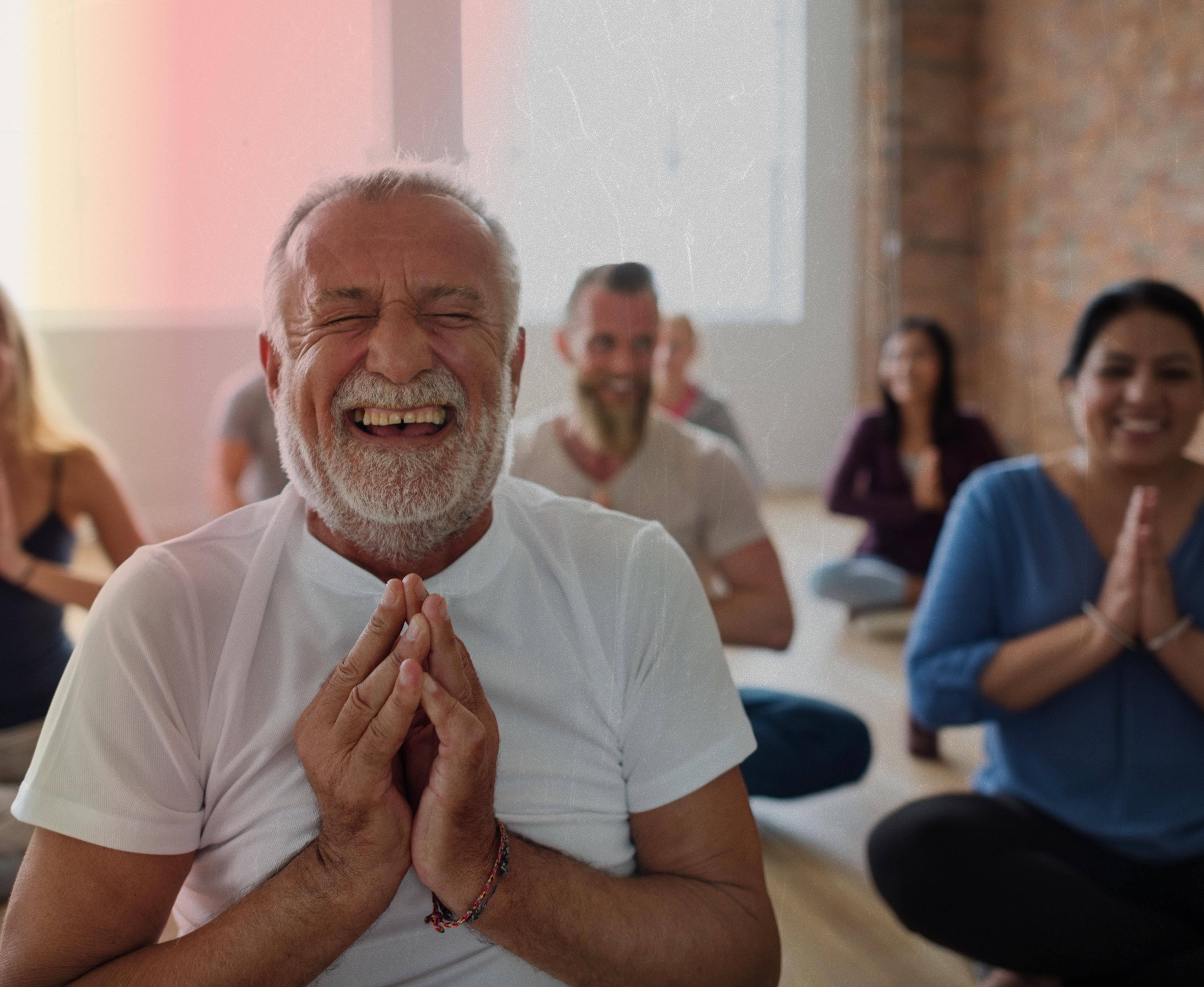 Man smiling and meditating in a room full of other people.