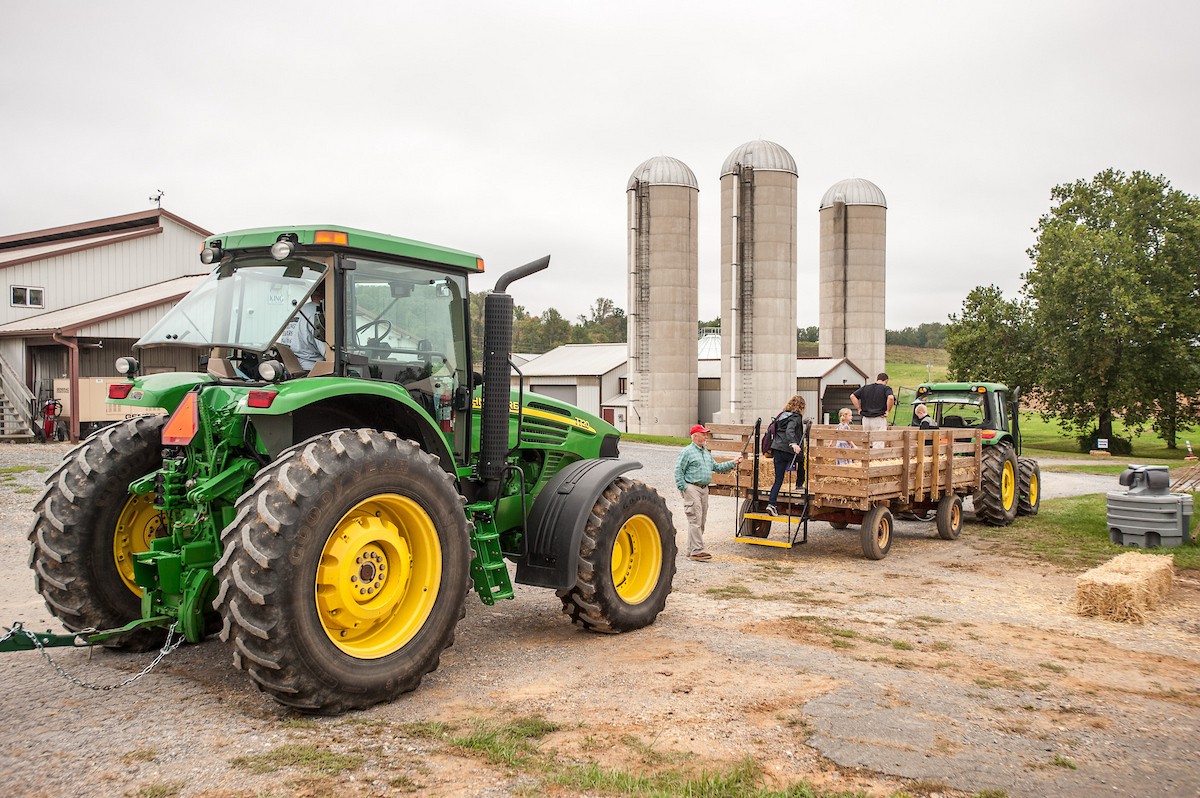 Green John Deere tractor with a trailer attached, outside of a farm.